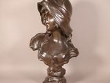 bronze bust of a woman with a hat on her head