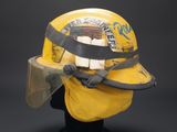 yellow fireman ' s helmet with face shield on display against a black background