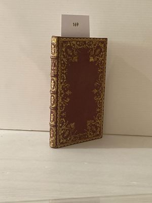 un petit livre rouge aux bords dorés posé sur une table blanche