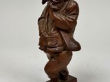 une statue en bois représentant un homme portant un chapeau et un sac