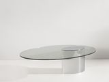 une table basse ovale en verre avec un piètement en métal dans une pièce blanche