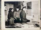 a black and white photo of a group of men standing around a table