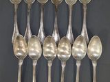 six cuillères en argent sont disposées en rangée sur une surface noire