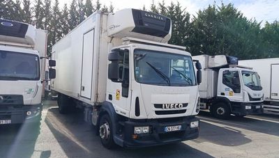 several white trucks are parked in a parking lot with trees in the background