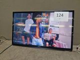 a flat screen tv sitting on a table with a couple of people in the background