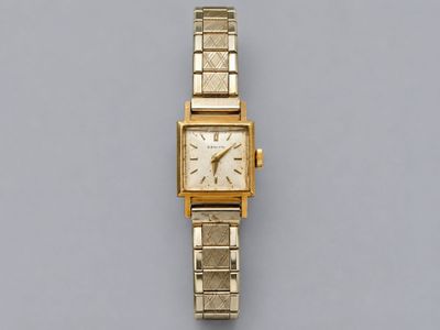 une image représentant une montre en or posée sur une surface grise