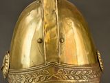 an antique brass helmet on a metal stand against a black background