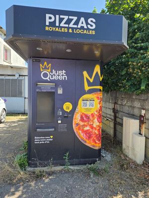 un distributeur automatique sur lequel est posée une pizza, devant un immeuble