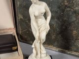 a statue of a woman standing on a marble base next to a pair of scissors