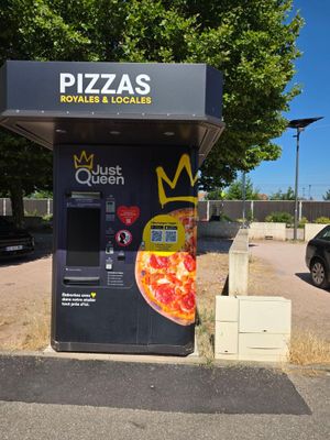 un distributeur automatique sur lequel est posée une pizza, au milieu d'un parking