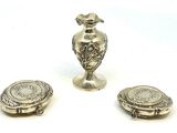 deux vases en argent et une petite assiette en argent posés sur un plan de travail blanc