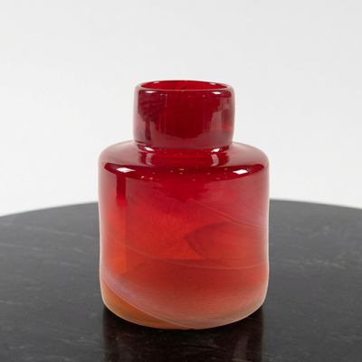 a red vase sitting on a black table with a white background