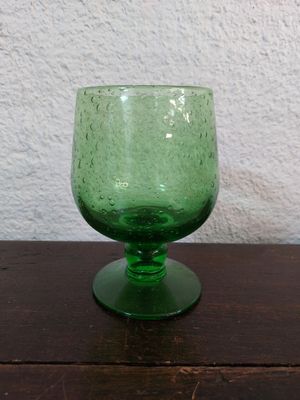 un verre vert posé sur une table, avec un mur blanc en arrière-plan