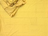 un lit avec une couverture jaune et une pile de vêtements pliés