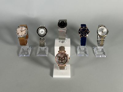 five different watches on display on a clear stand
