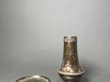 a small silver vase next to a plate on a table