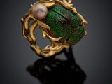 a close up of a gold ring with a green beetle and a pearl