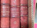 several old books are stacked in a cardboard box on a shelf