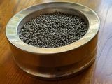 a metal bowl filled with black seeds on a wooden table