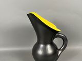 un vase noir avec un couvercle jaune posé sur une surface grise