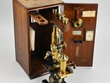 un vieux microscope avec un étui en bois et une poignée en métal