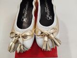 une paire de chaussures blanches ornées de nœuds dorés, posée sur une boîte rouge