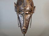 an image of a bronze mask on a stand against a white wall