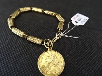 Gros plan sur un bracelet en or orné d'une pièce de monnaie