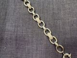 un gros plan d'un bracelet à maillons dorés posé sur un tissu gris