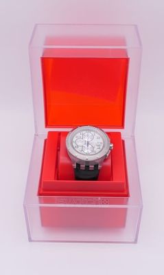 une montre dans une boîte transparente posée sur une surface blanche