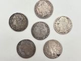 six types différents de pièces d'argent sur une surface blanche