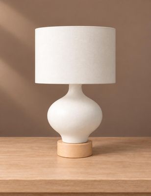 une lampe blanche posée sur une table en bois, près d'un mur marron