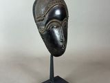 a bronze mask on a black stand with a white background