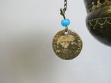 a gold coin with a blue bead hanging from a chain
