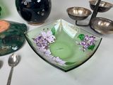 a green bowl with purple flowers on it next to other bowls and spoons
