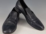 une paire de pantoufles en cuir noir pour homme posées sur une surface blanche