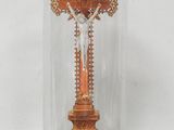 une croix richement décorée, placée sous un dôme en verre et reposant sur un socle en bois