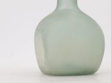 a green glass bottle sitting on a white surface
