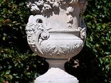 a stone vase sitting on a pedestal in front of a bush
