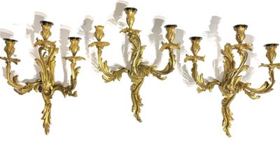 three gold colored metal wall sconces with candles on each of them