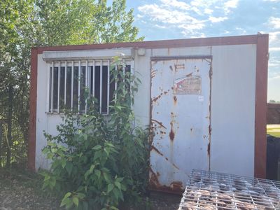 un bâtiment rouillé, à côté d'une clôture et d'une poubelle