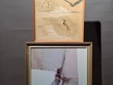 two framed paintings on a wooden stand with a painting of a bird on it