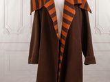 an orange and brown coat on a mannequin stand in front of a white wall
