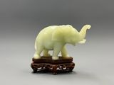 une statue d'éléphant posée sur un socle en bois, avec un fond gris en arrière-plan