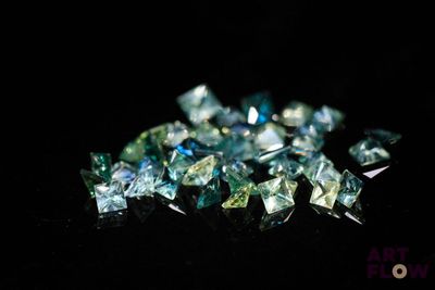 a close up of a pile of blue and green diamonds on a black surface