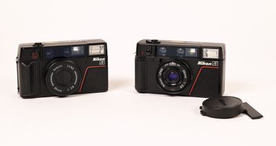 two cameras sitting next to each other on a white surface