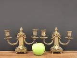 candlesticks and an apple on a table against a gray wall