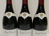 trois bouteilles de vin rouge sont alignées sur une surface blanche