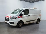 La camionnette blanche est garée dans une grande pièce ; elle porte une bande rouge et blanche sur le côté.