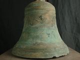 une grande cloche posée sur un socle, avec un drapeau en arrière-plan